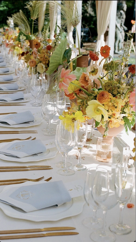 Close-up of a long wedding table beautifully decorated with vibrant floral arrangements, elegant tableware, and gold cutlery.